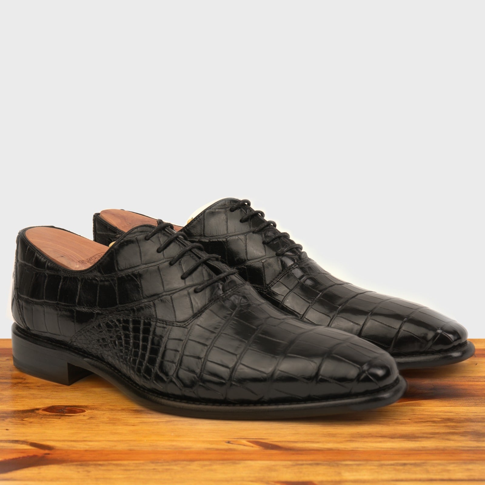 A Pair of Black crocodile leather shoe on a wooden surface with a light gray background
