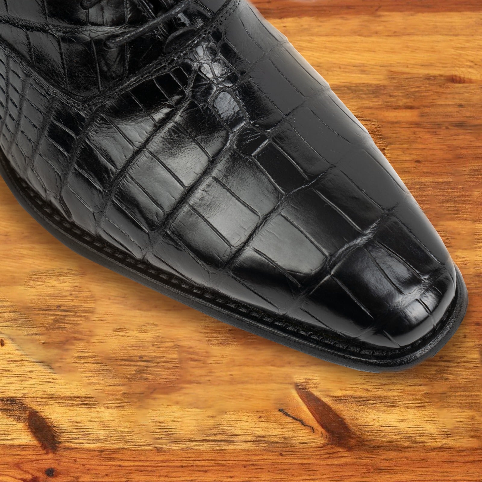 Black crocodile leather shoe on a wooden surface