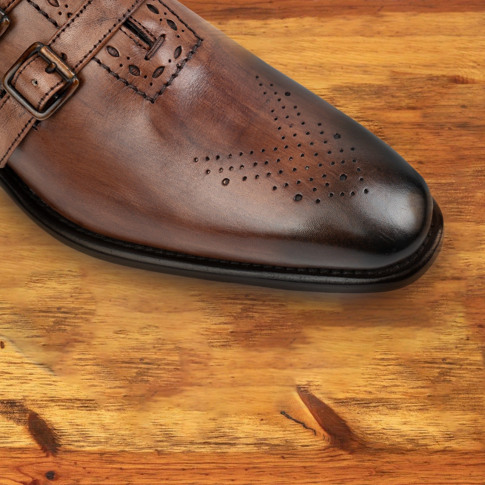 Brown leather shoe with double buckles on a wooden surface