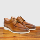 A pair of Brown leather shoe on a wooden surface with a light gray background