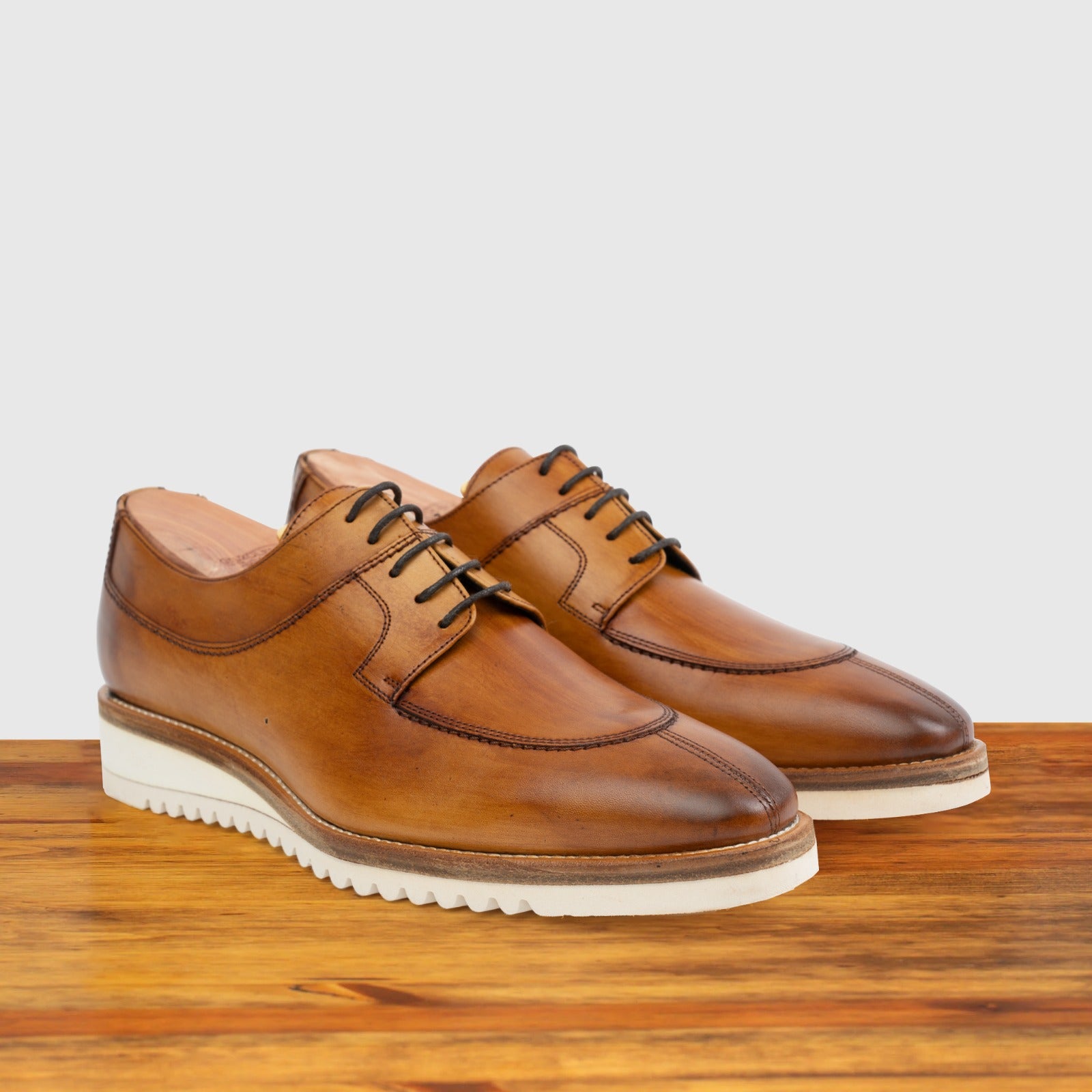 A pair of Brown leather shoe on a wooden surface with a light gray background