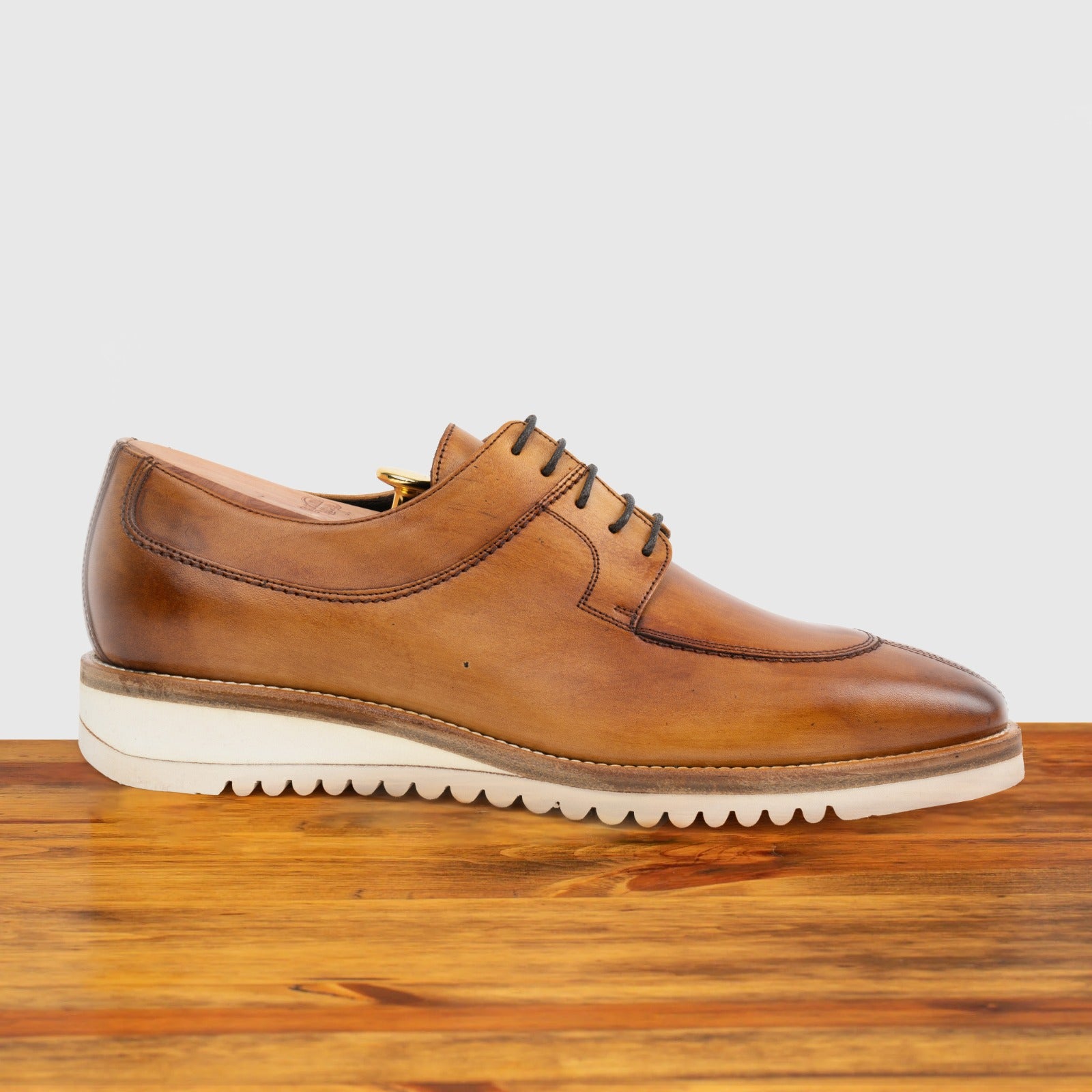 Brown leather shoe on a wooden surface with a light gray background