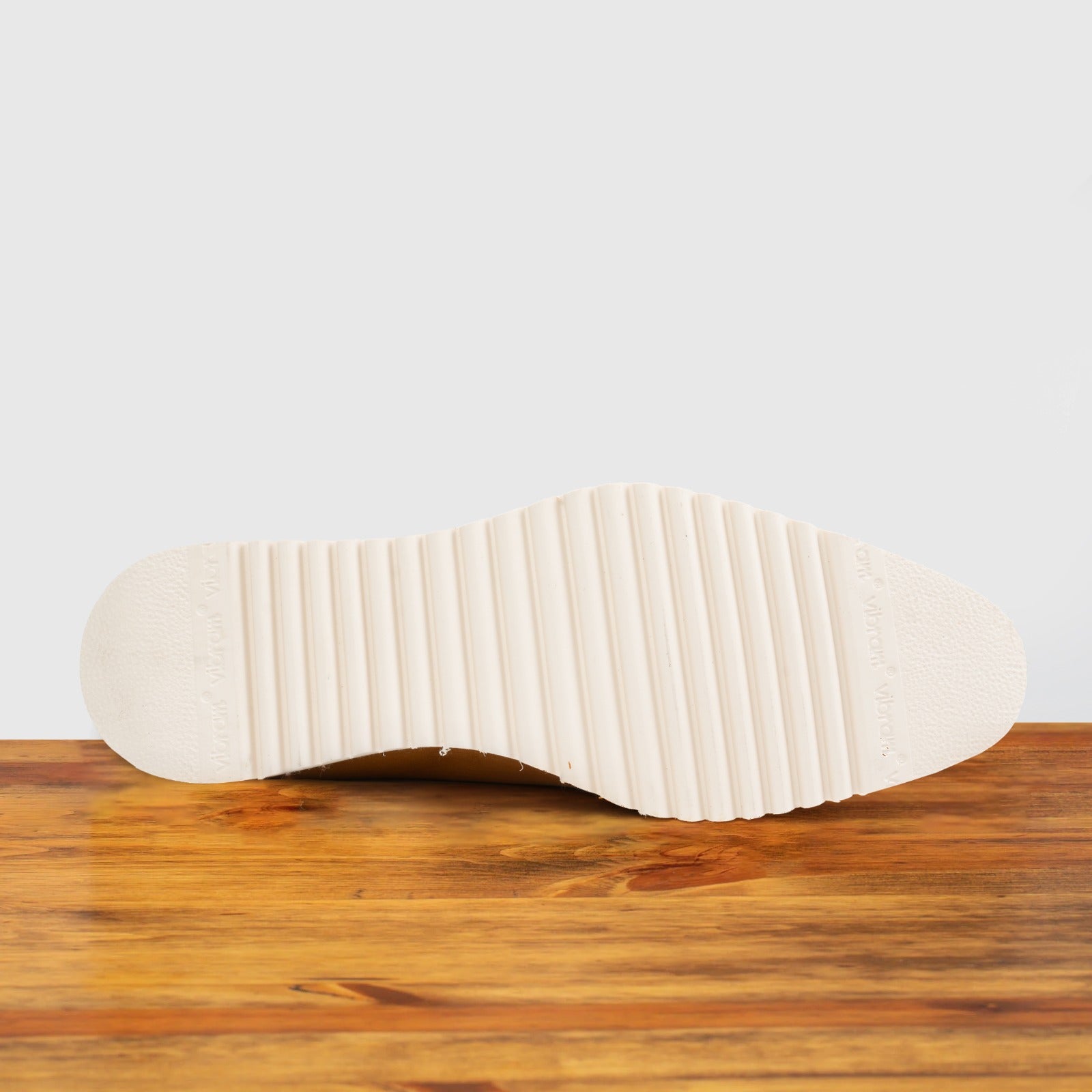 Outsole of Brown leather shoe on a wooden surface with a light gray background