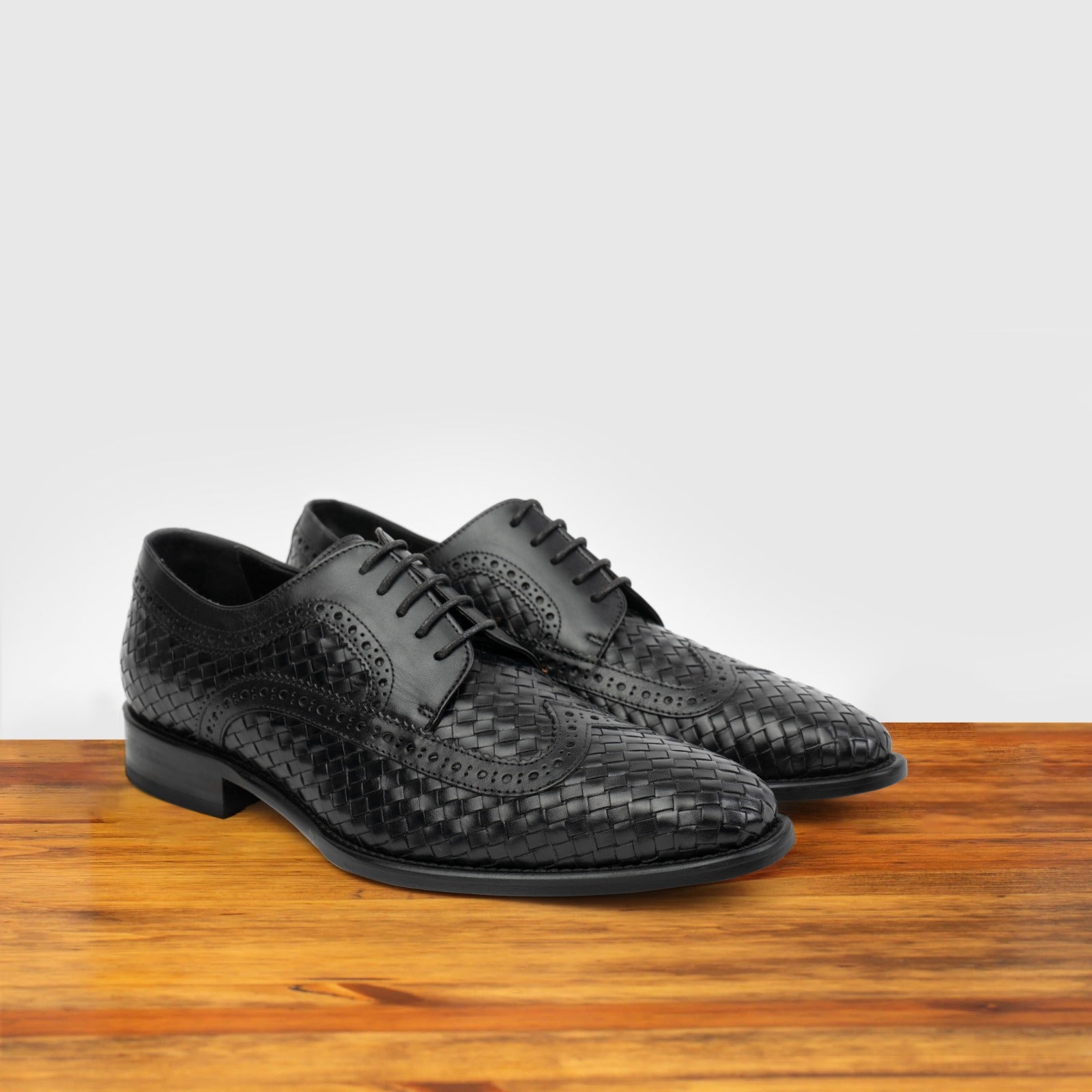  A pair of Black woven dress shoe on a wooden surface with a light gray background