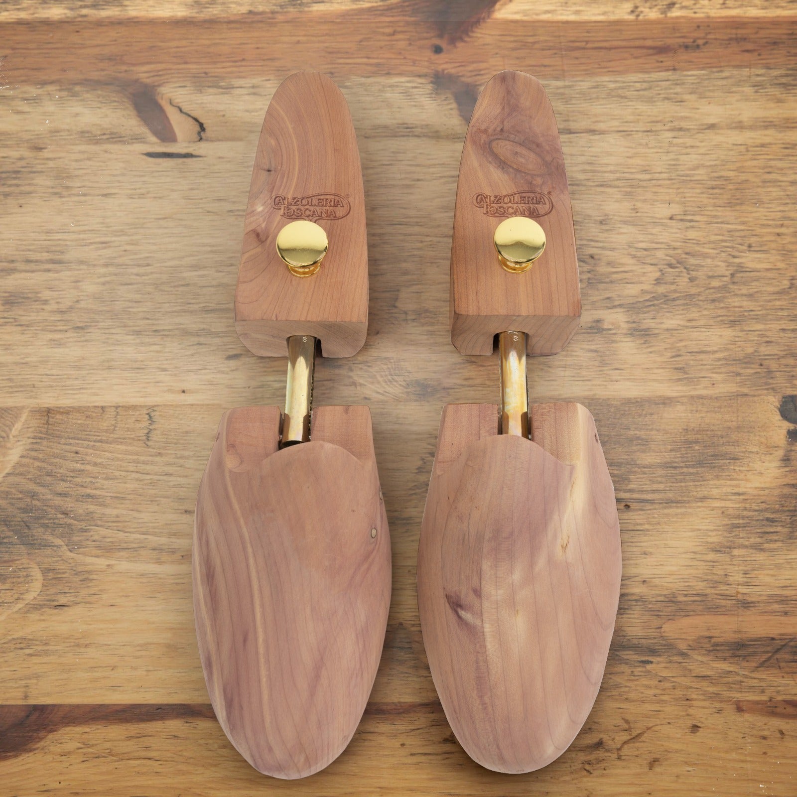 Pair of wooden shoe trees with brass adjustment knobs and metal shafts, displayed side by side on a wooden surface.