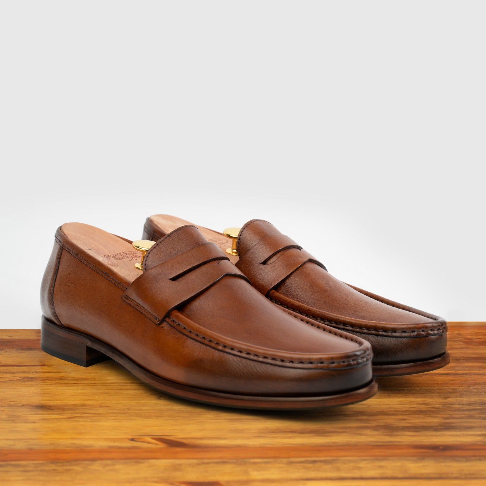 A Pair of Dark Caramel leather loafer on a wooden surface with a light gray background