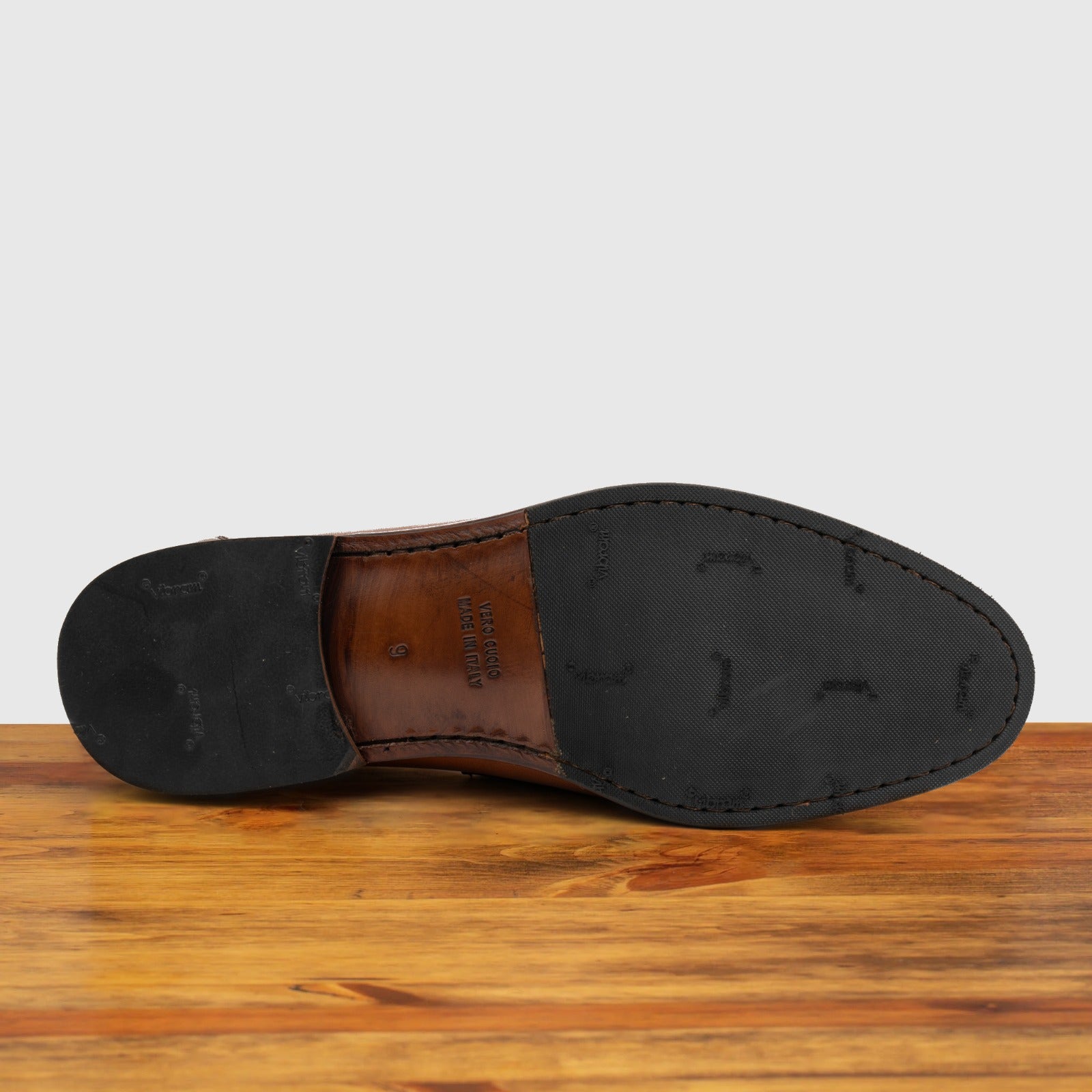 Outsole of Dark Caramel leather loafer on a wooden surface with a light gray background