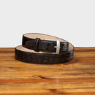 A brown genuine exotic hornback belt with a silver buckle on a wooden surface.