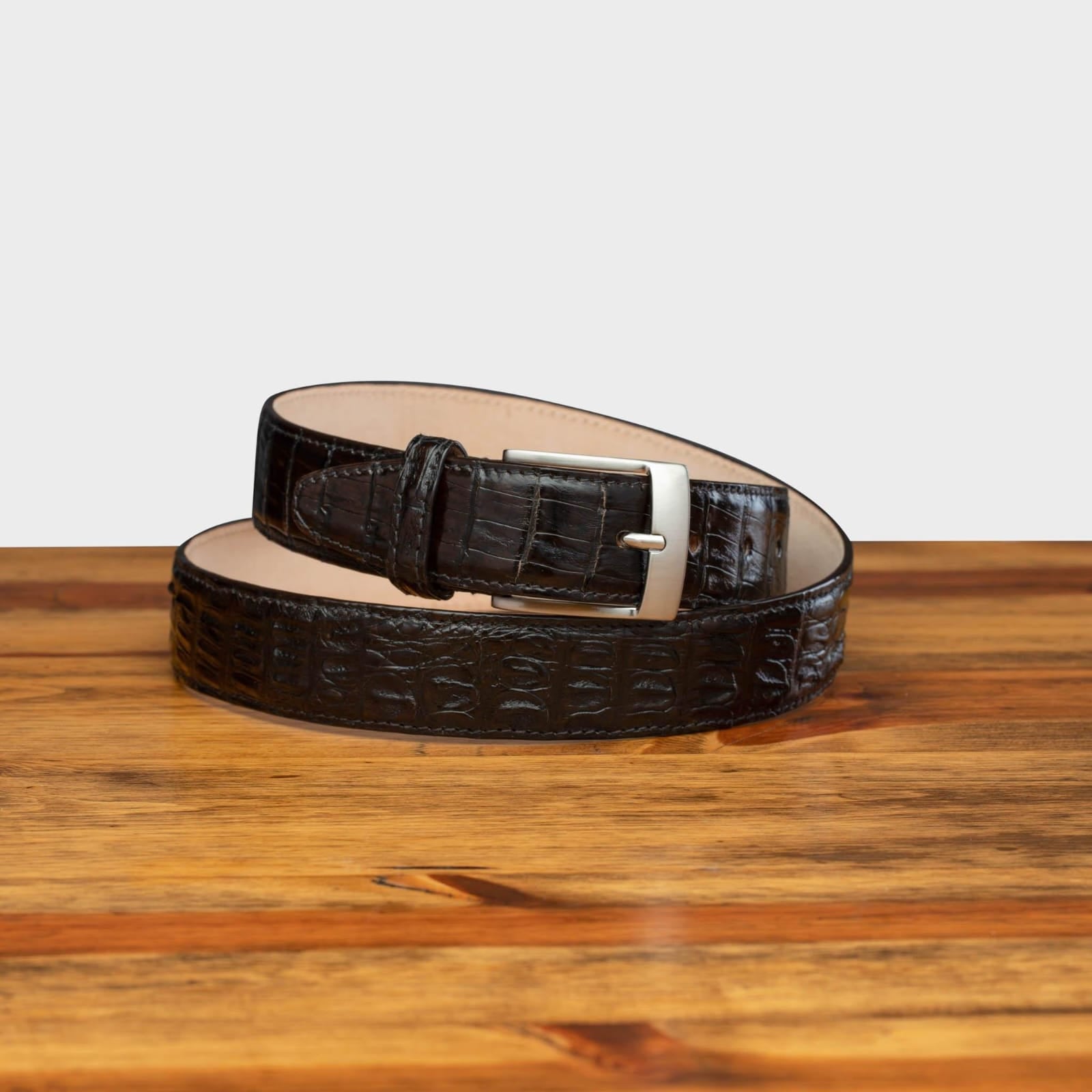 A brown genuine exotic hornback belt with a silver buckle on a wooden surface.