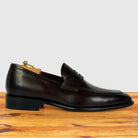 A Burgundy leather penny loafer shoe with a low stacked heel, displayed on a wooden surface against a light gray background.
