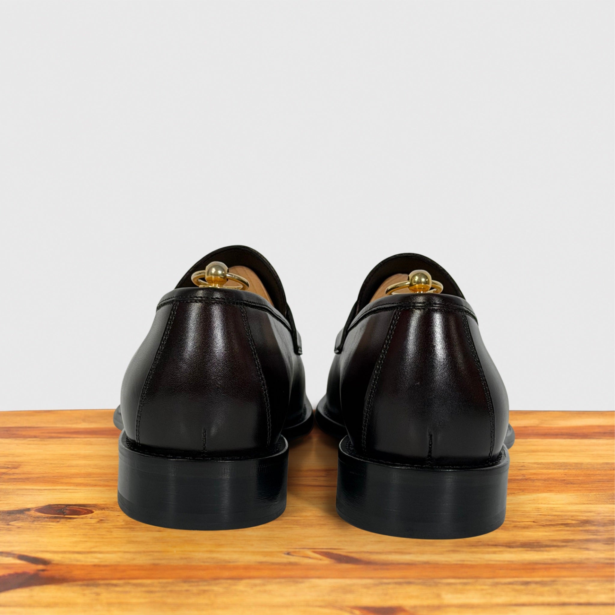 A pair of Burgundy leather loafers shown from the back, resting on a wooden surface against a light gray background.