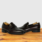 A pair of Burgundy leather penny loafers with black soles, on a wooden surface against a light gray background.