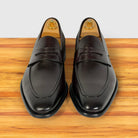 A pair of men's Burgundy leather penny loafers with a glossy finish, displayed on a wooden surface with wooden shoe trees visible inside.