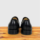 A pair of Graphite leather loafers shown from the back, resting on a wooden surface against a light gray background.