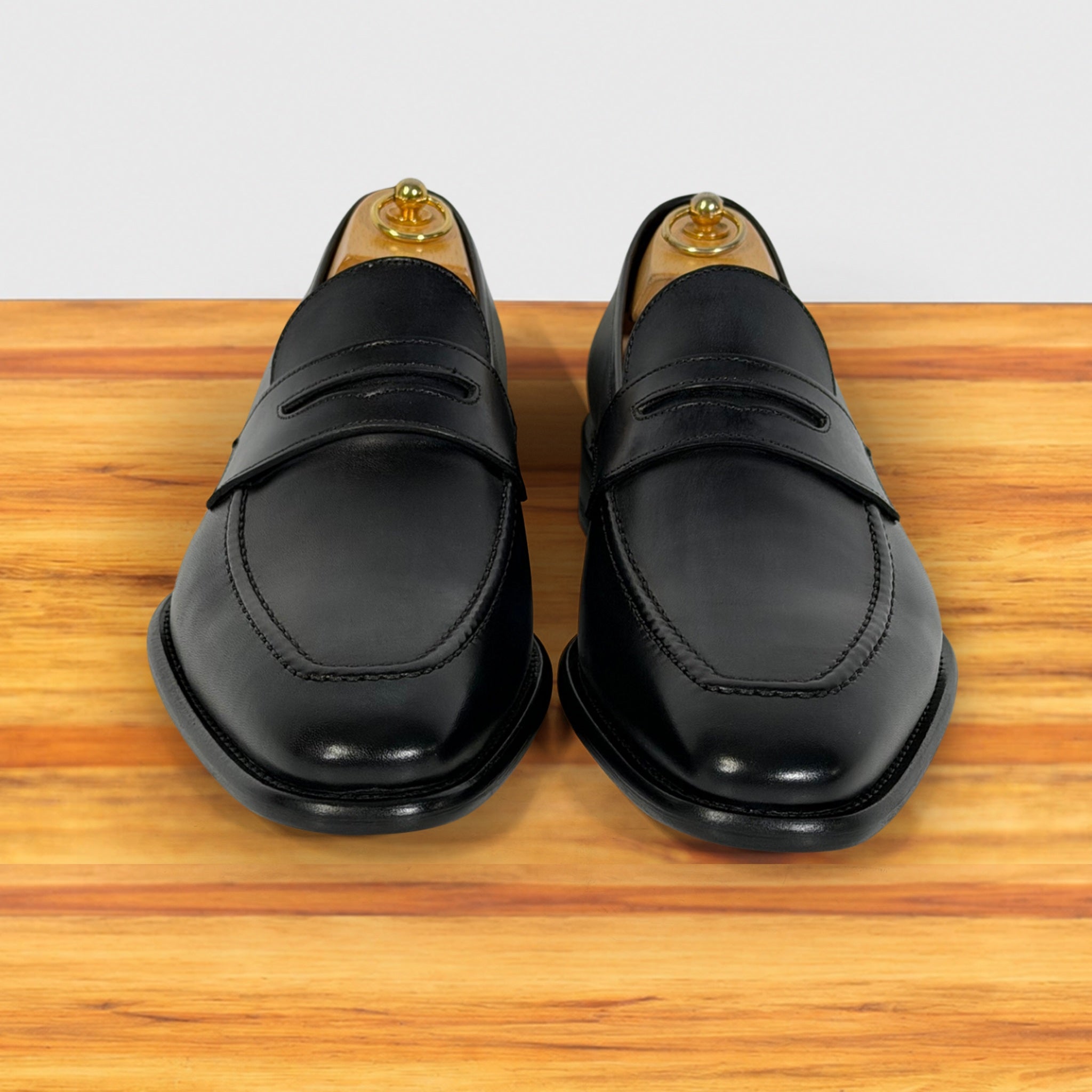 A pair of Graphite leather penny loafers, on a wooden surface against a white background.