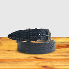 Black textured belt with silver buckle on a wooden surface