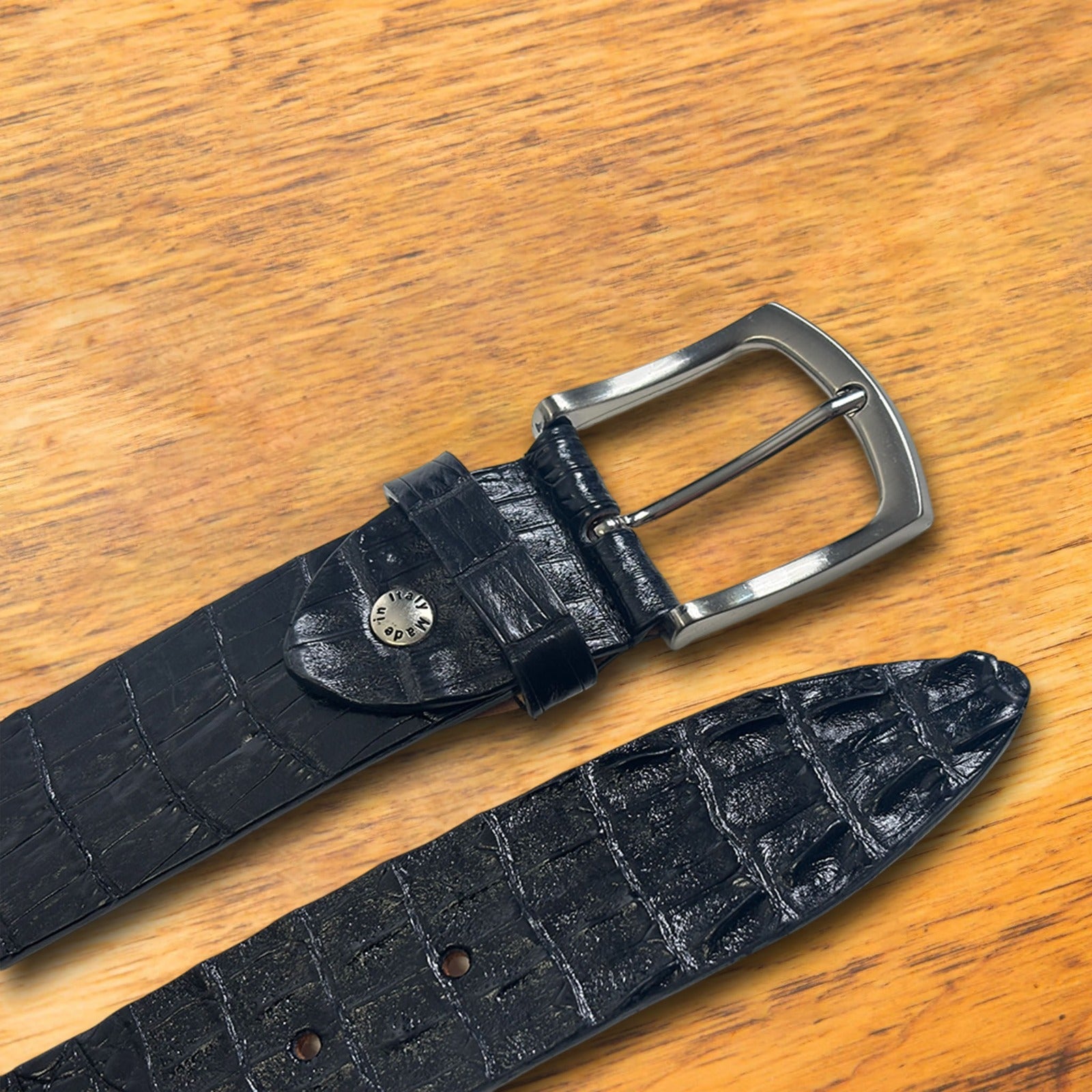 Black textured belt with silver buckle on a wooden surface
