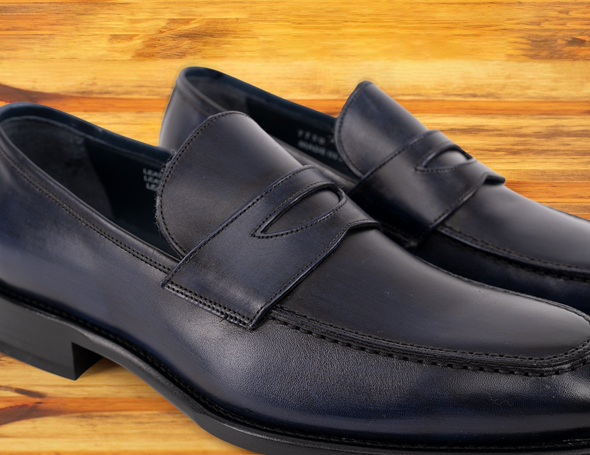 A Pair of blue Italian leather dress loafer with a penny strap, on a wooden surface.