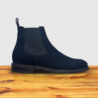 Navy blue Chelsea boot on a wooden surface with a light gray background