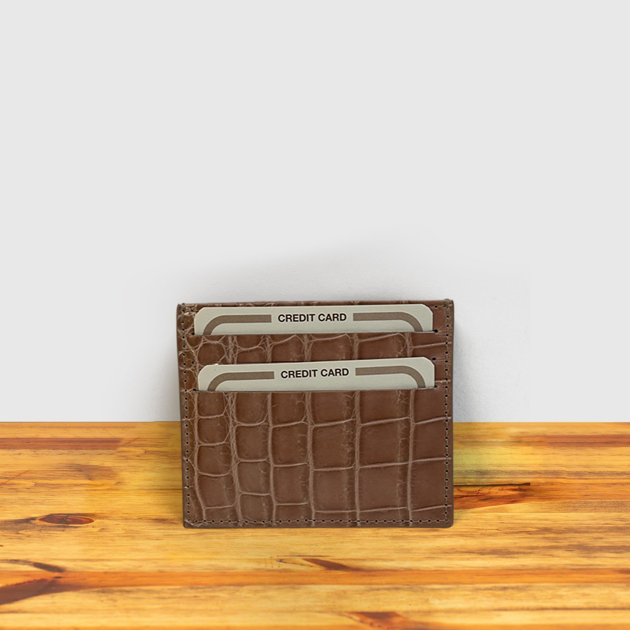 Blush crocodile-patterned cardholder with credit cards on a wooden surface and light gray background