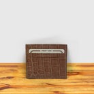 Blush crocodile-patterned cardholder with credit card a on a wooden surface and light gray background