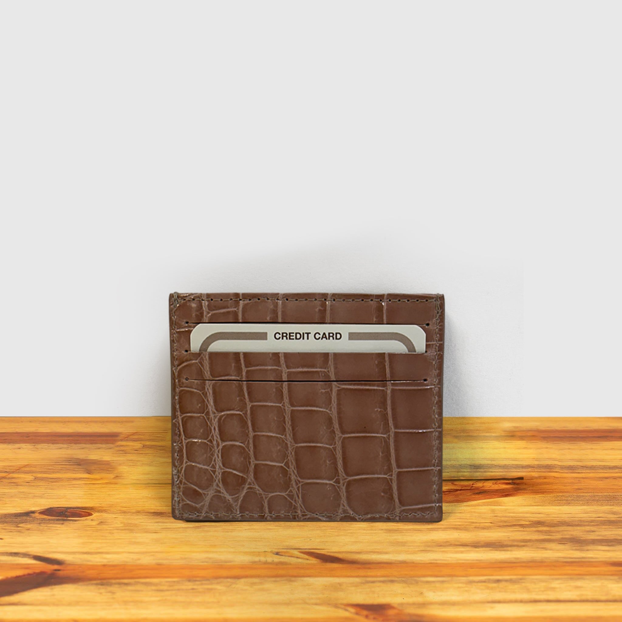 Blush crocodile-patterned cardholder with credit card a on a wooden surface and light gray background