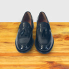 Pair of black loafers with tassels on a wooden surface