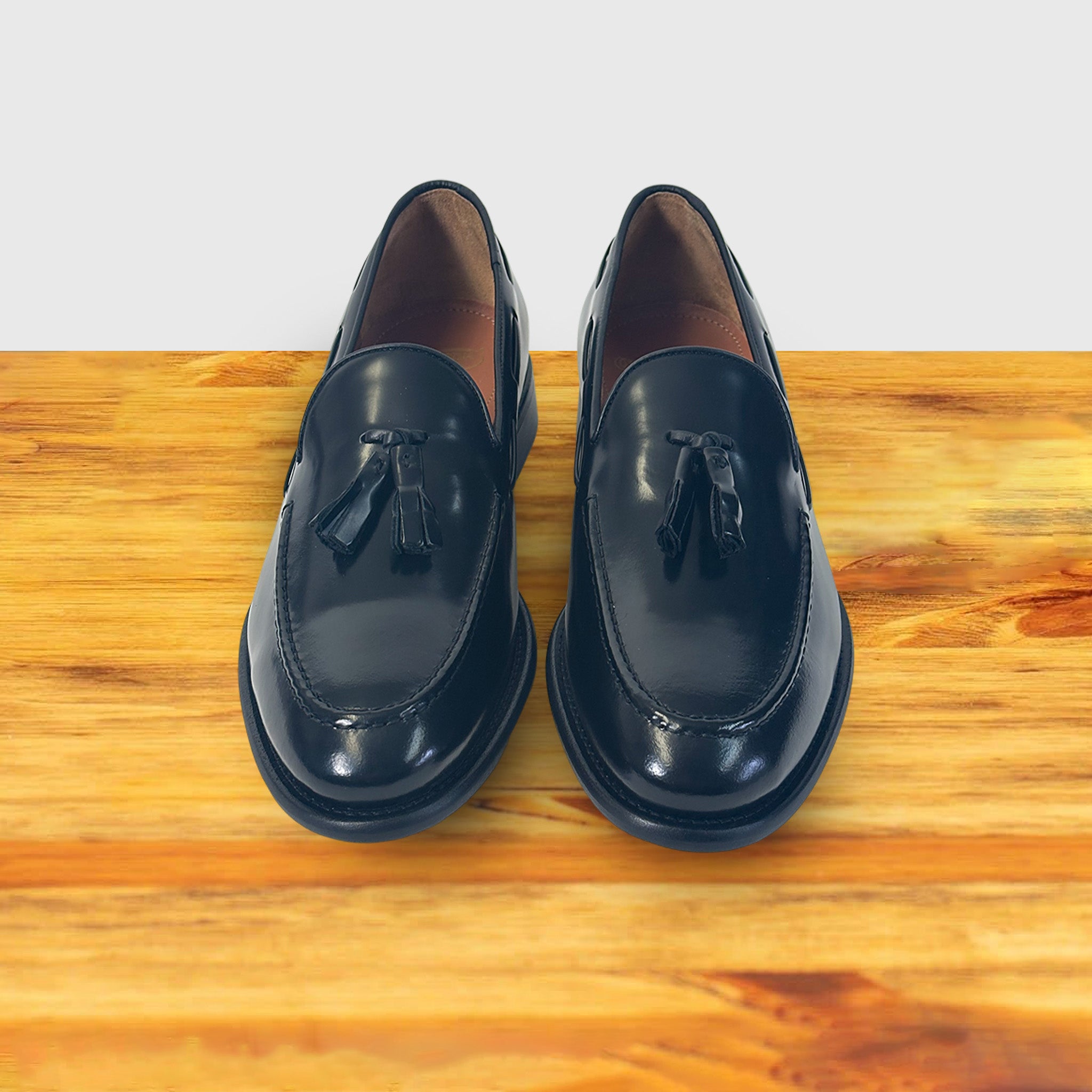 Pair of black loafers with tassels on a wooden surface