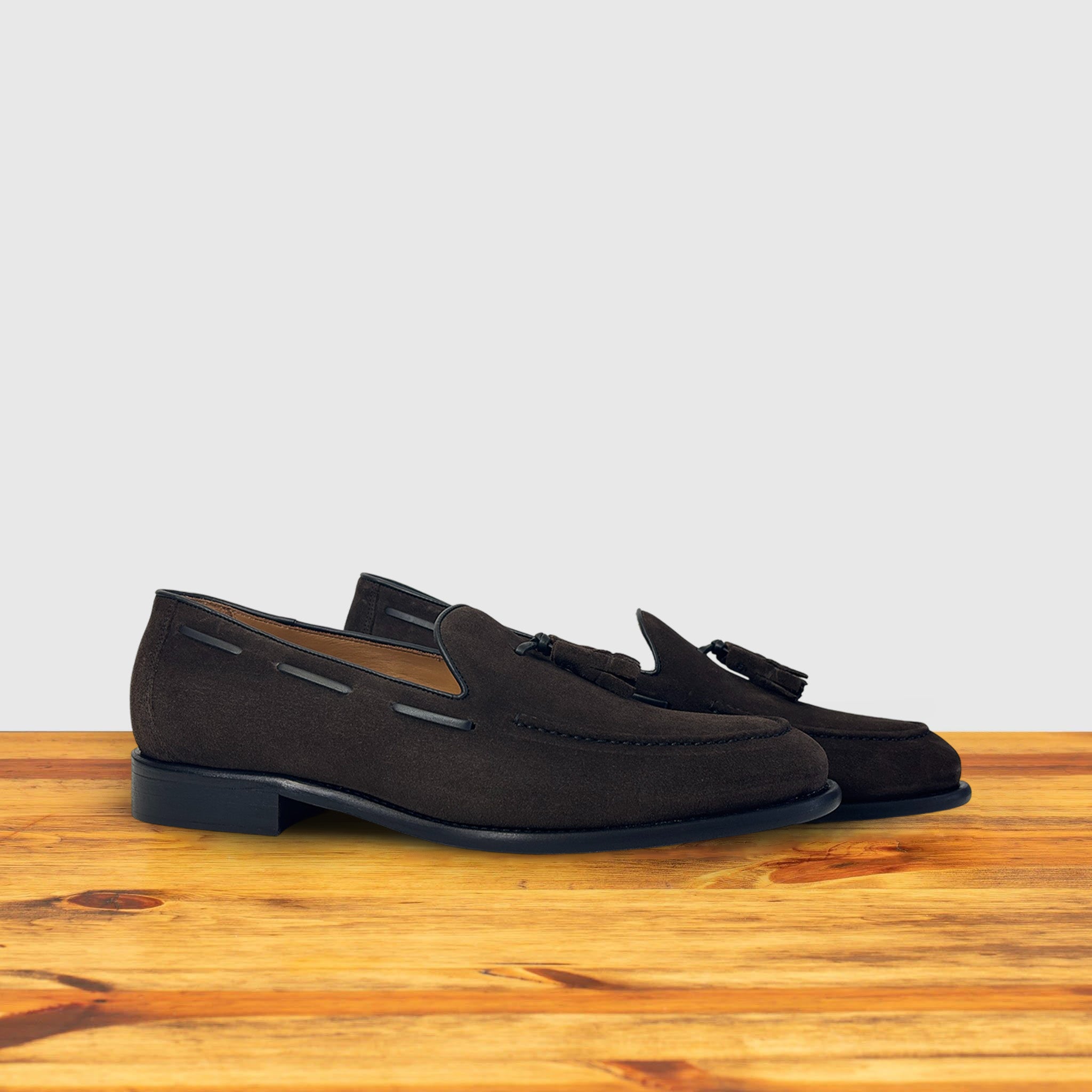 A Pair of Dusty Brown loafer with a tassel placed on a wooden surface.