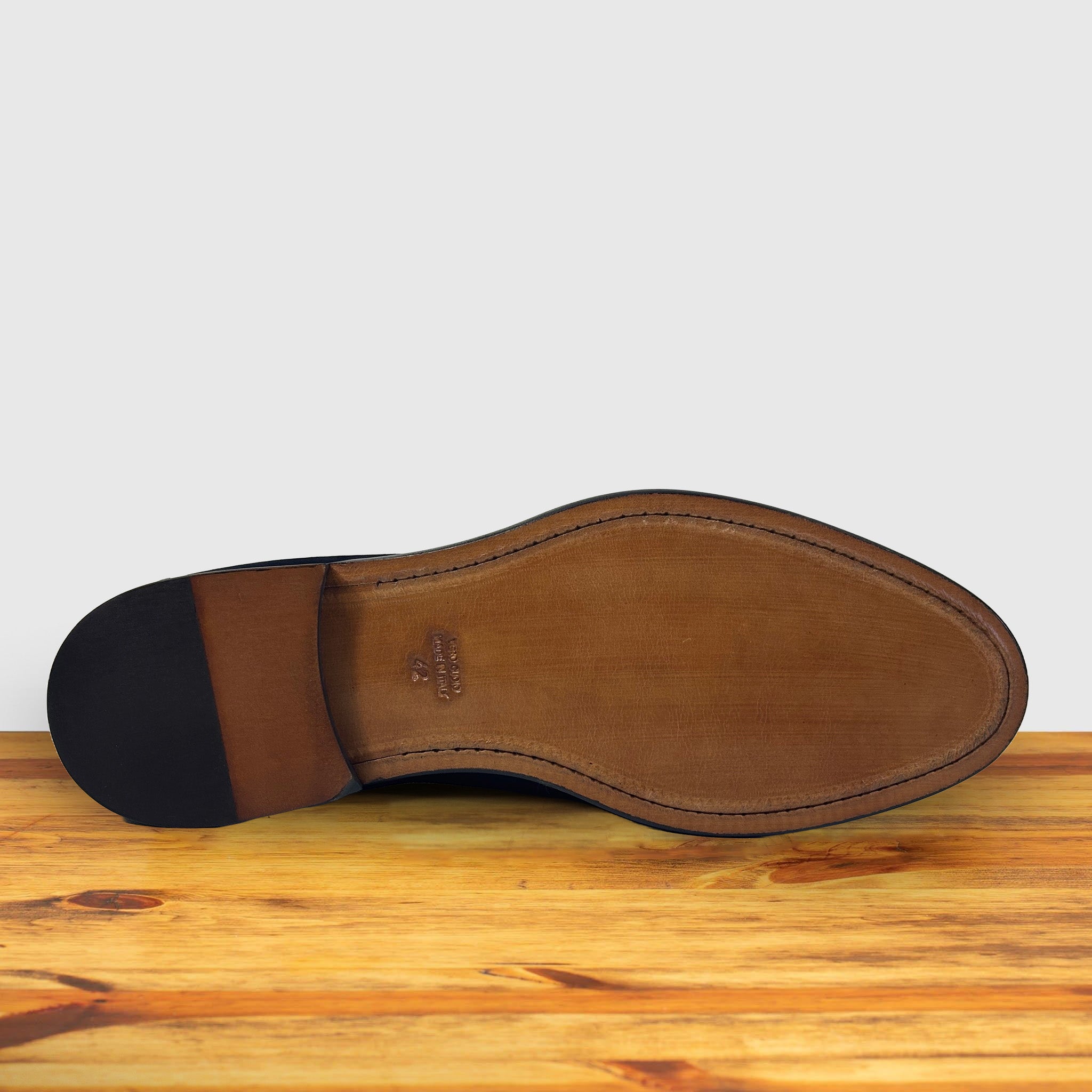 Outsole of Dusty Brown loafer placed on a wooden surface.