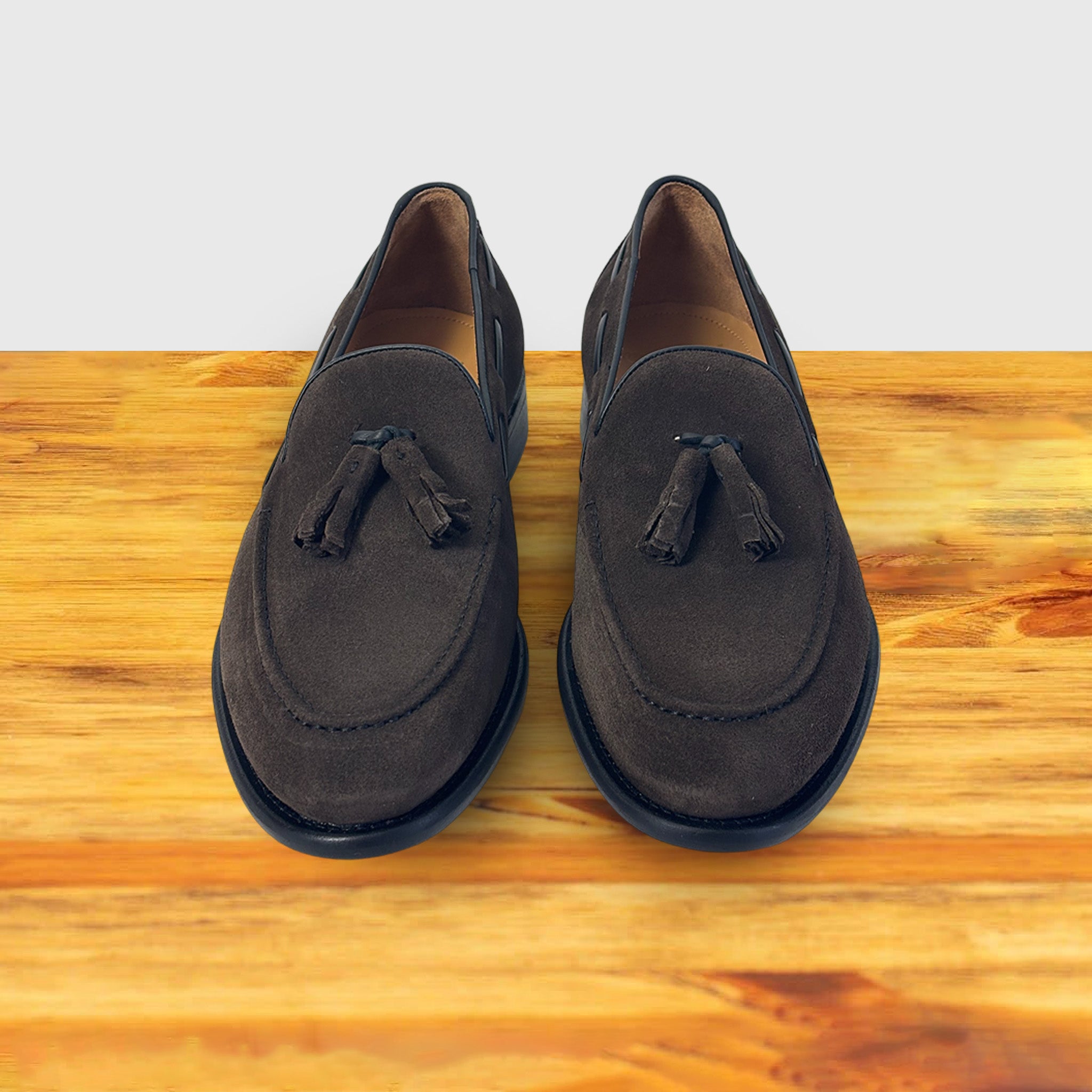 A Pair of Dusty Brown loafer with a tassel placed on a wooden surface.