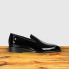 Black patent leather loafer on a wooden surface with a light gray background