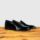 A Pair of Black patent leather loafer on a wooden surface with a light gray background