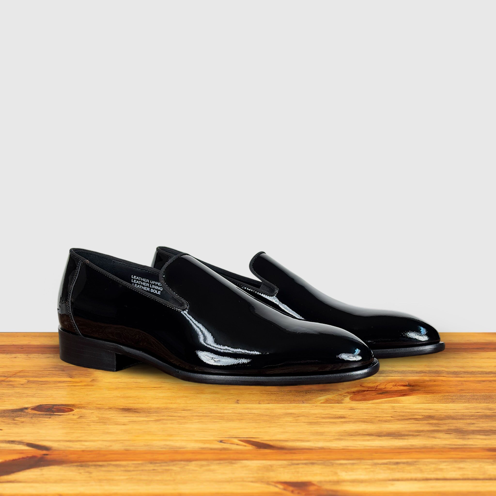 A Pair of Black patent leather loafer on a wooden surface with a light gray background