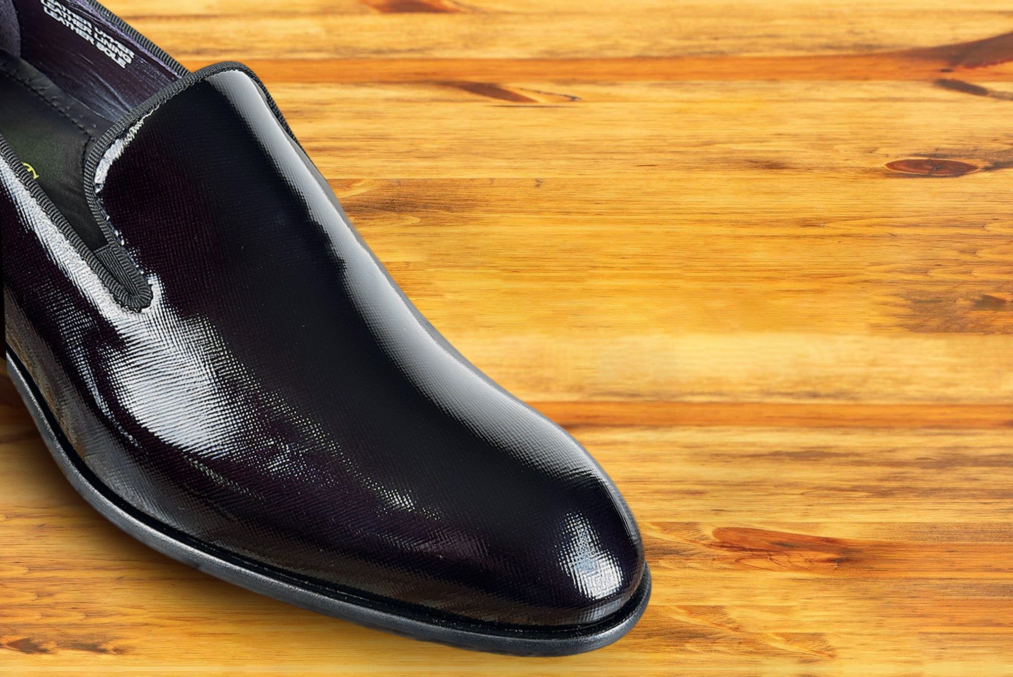 Burgundy patent leather loafer on a wooden surface