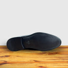 Outsole of Black patent leather loafer on a wooden surface with a light gray background