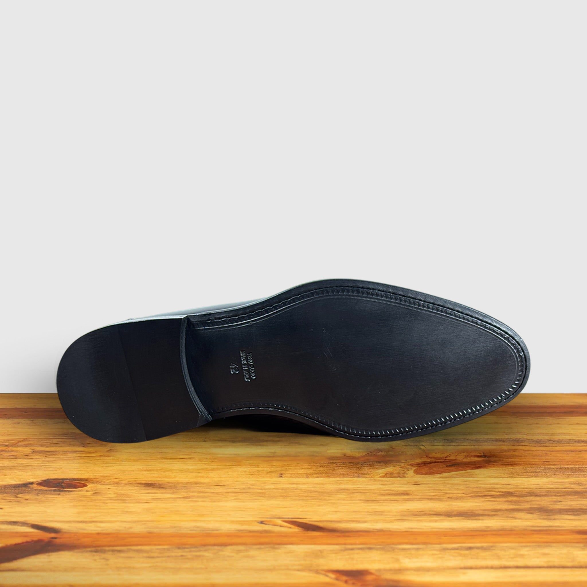 Outsole of Black patent leather loafer on a wooden surface with a light gray background