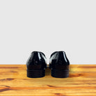 A Pair of Black patent leather loafer on a wooden surface with a light gray background