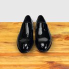 A Pair of Black patent leather loafer on a wooden surface with a light gray background