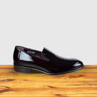 A single Burgundy patent leather slip-on shoe placed on a wooden surface, with a polished finish and a low heel.