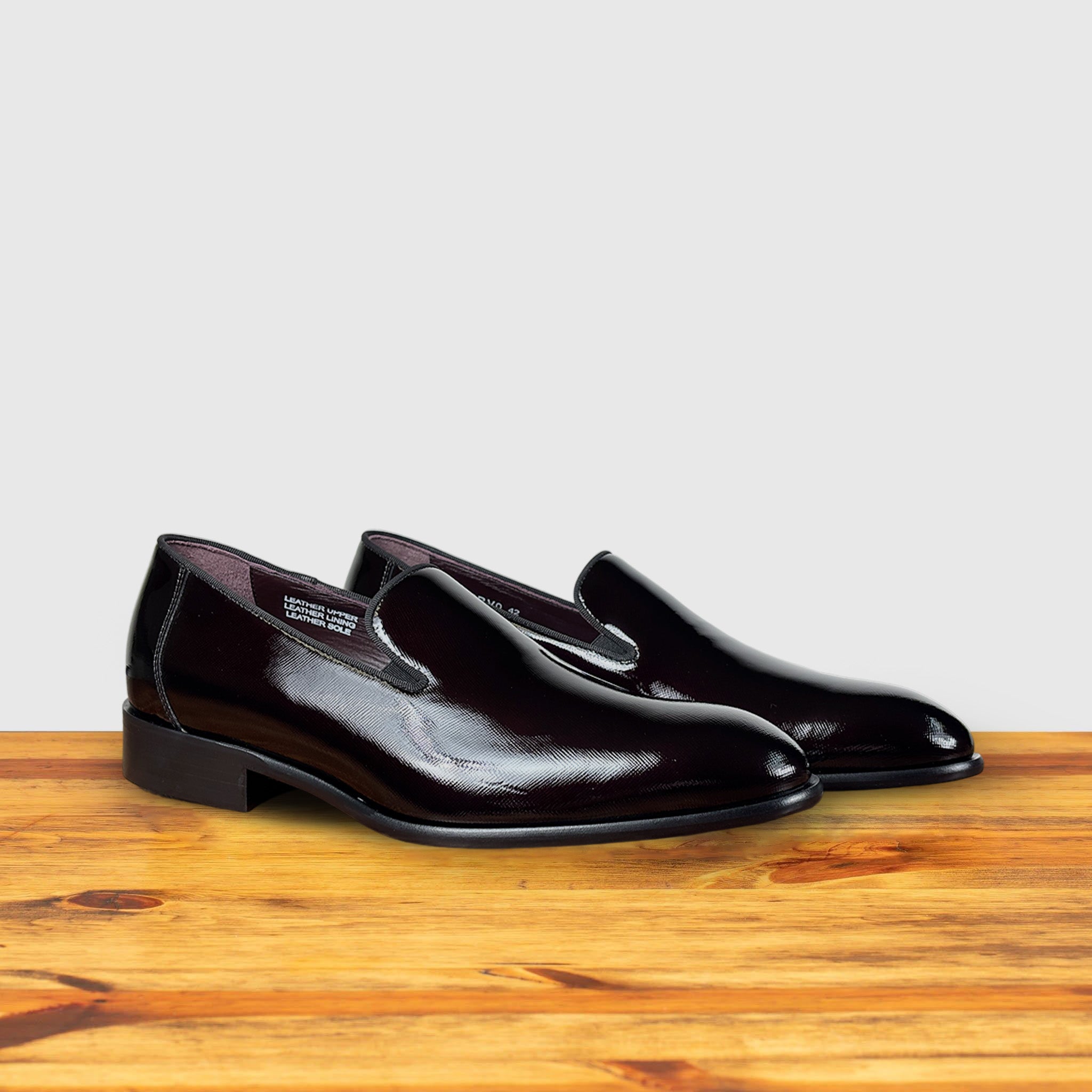 A Pair of burgundy patent leather loafer on a wooden surface with a light gray background