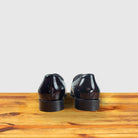 A Pair of burgundy patent leather loafer on a wooden surface with a light gray background