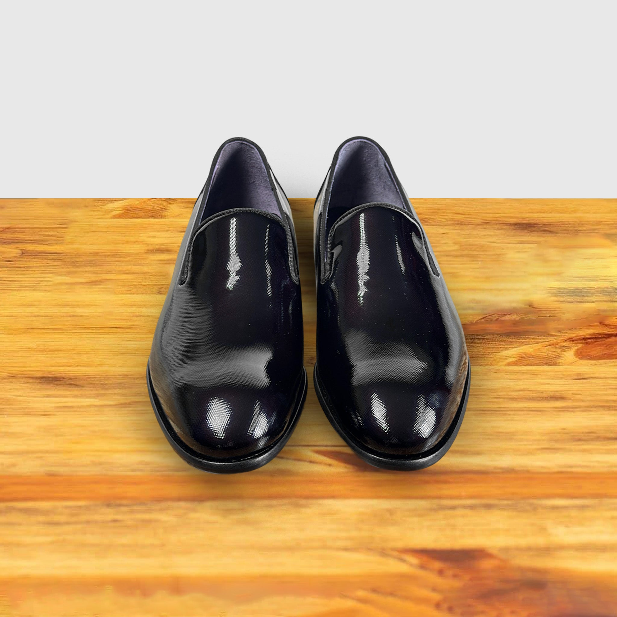A Pair of burgundy patent leather loafer on a wooden surface with a light gray background