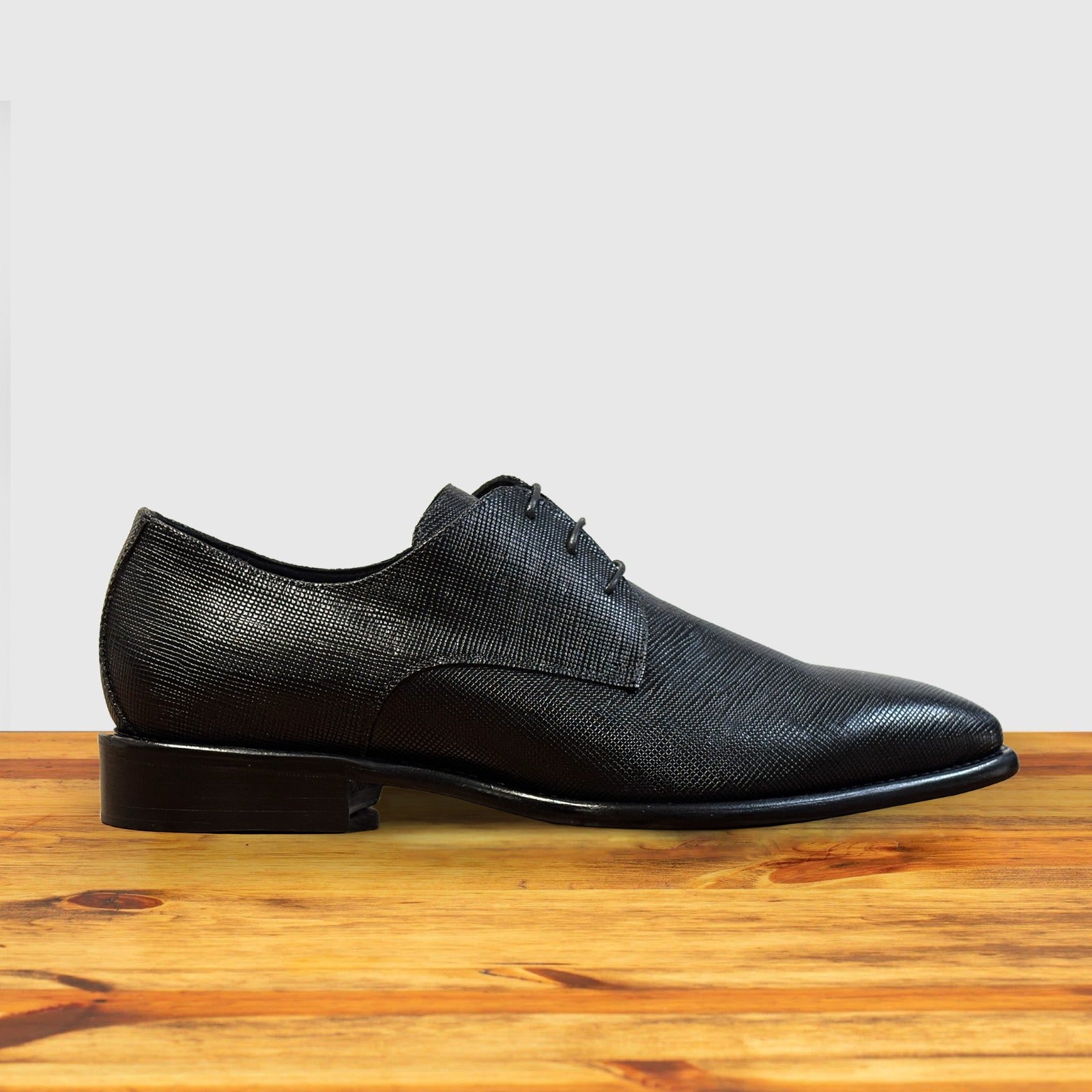 Black leather dress shoe on a wooden surface with a light gray background