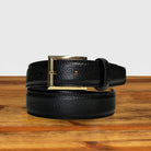 Black leather belt with a gold buckle on a wooden surface