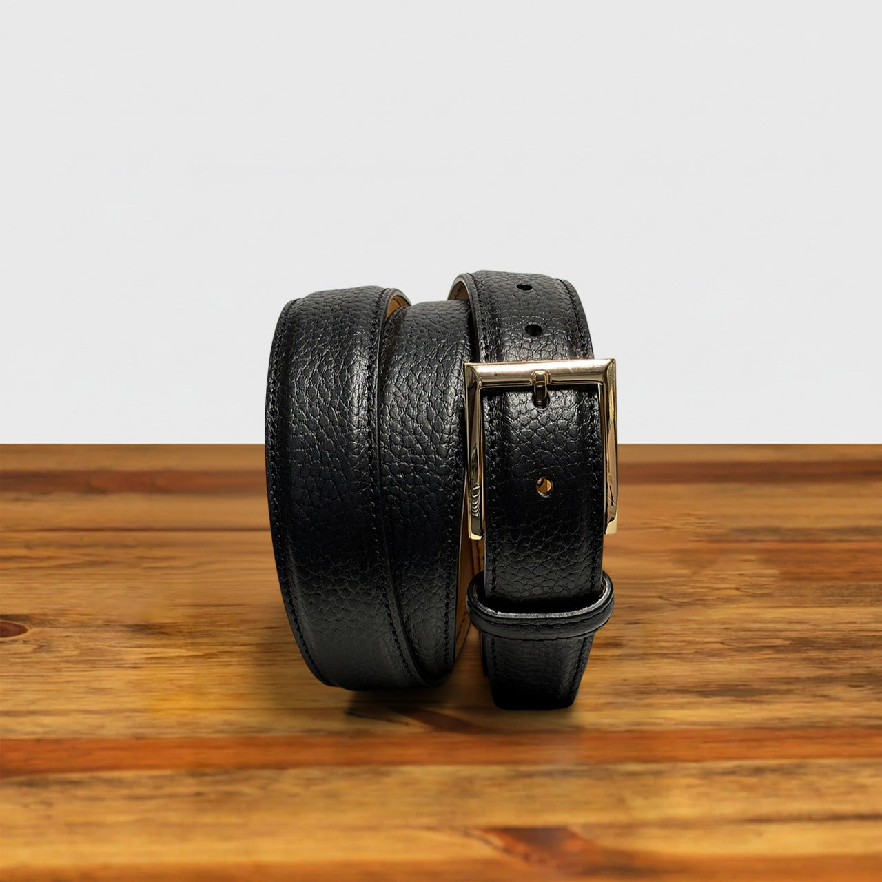 Black leather belt with gold buckle on a wooden surface
