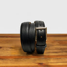 Black leather belt with gold buckle on a wooden surface