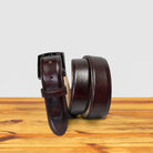 Burgundy leather belt on a wooden surface with a light gray background