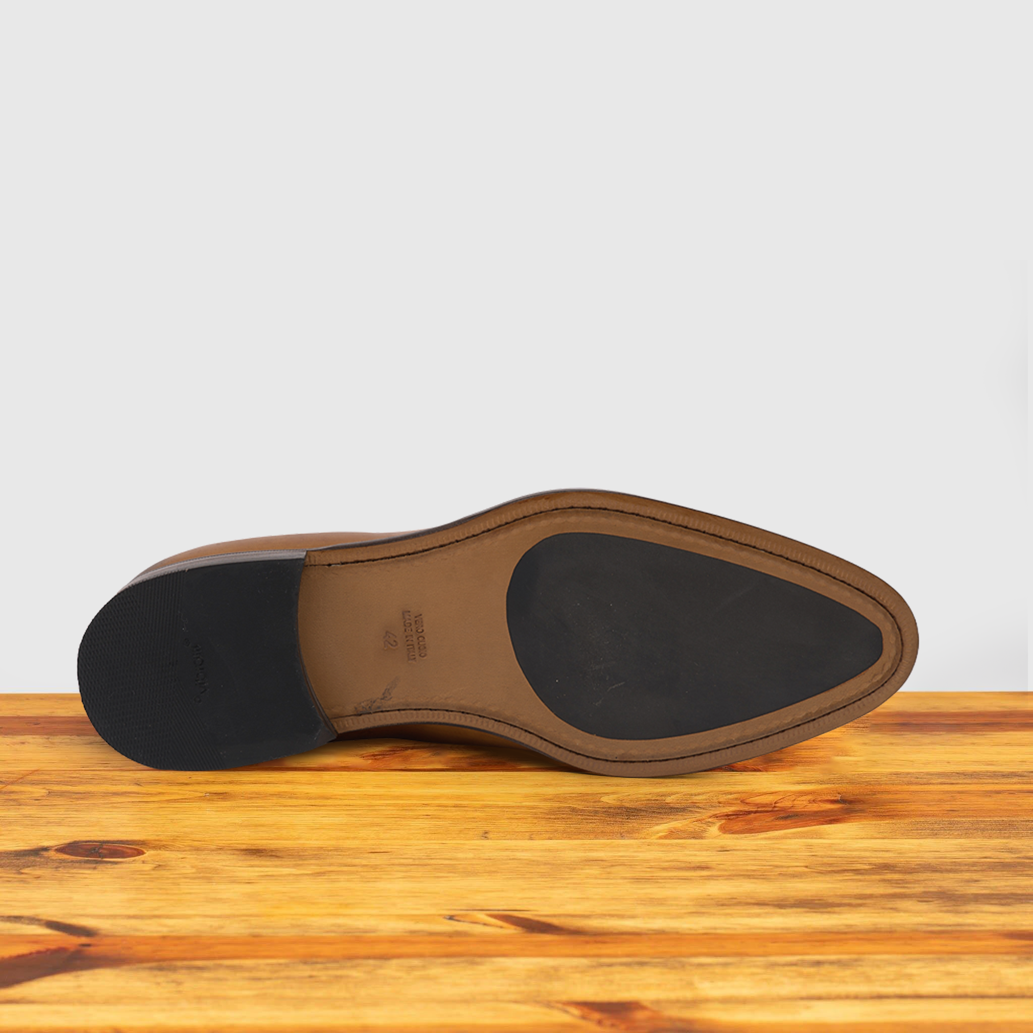 Outsole of Brown leather loafer on a wooden surface with a light gray background