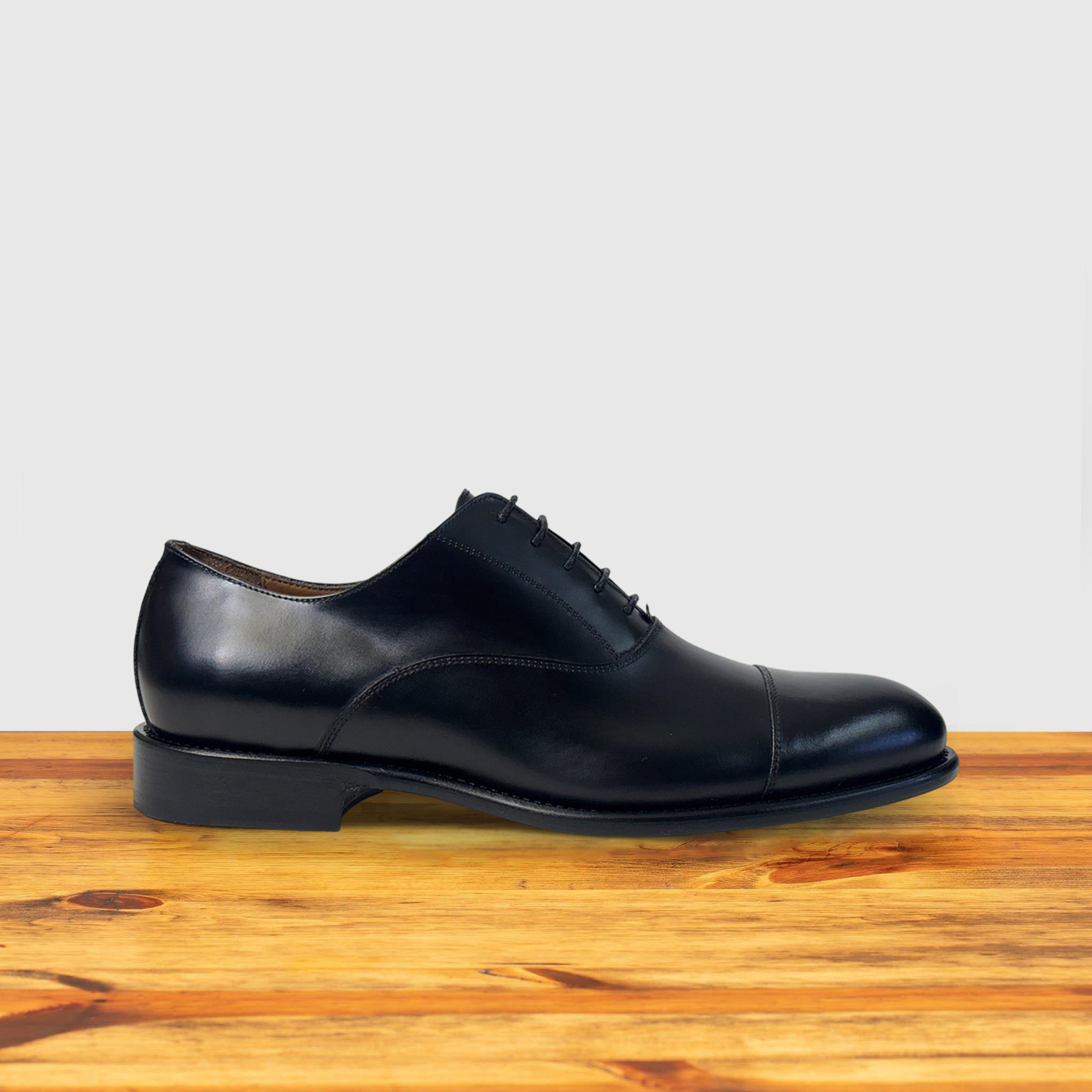 Black leather dress shoe on a wooden surface with a light gray background
